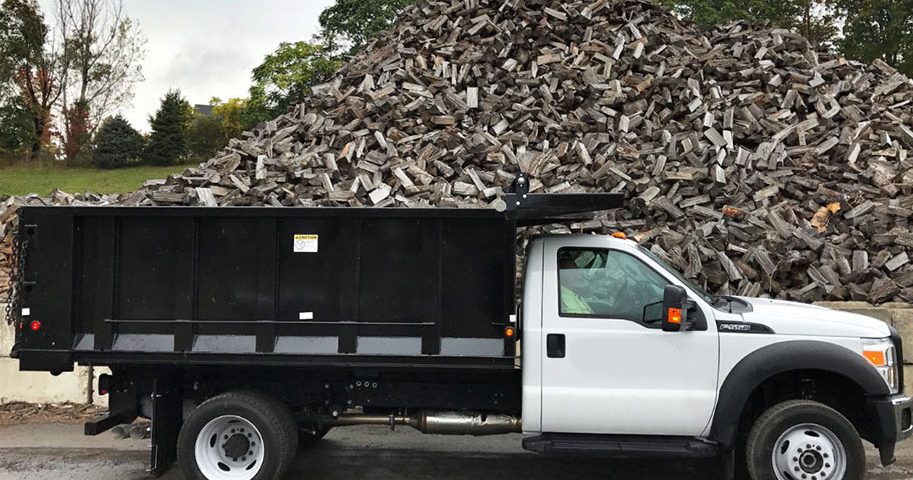 A truck is parked in front of a pile of wood.