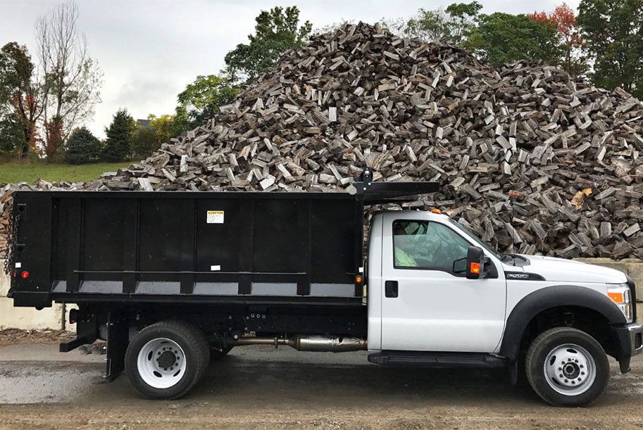 A truck is parked in front of a pile of wood.
