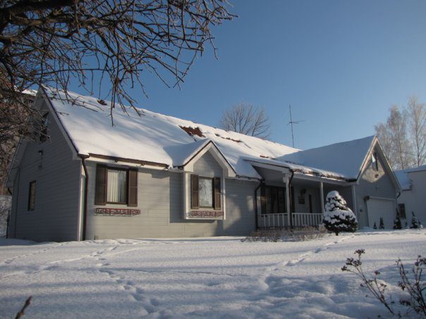 A house with snow on the roof and trees in front of it.