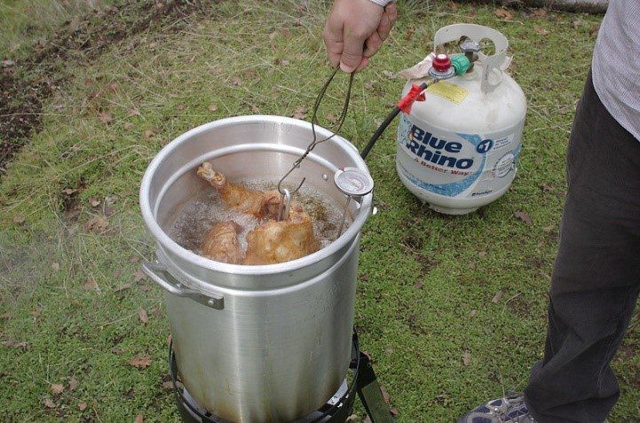 A person is cooking chicken in an outdoor pot.